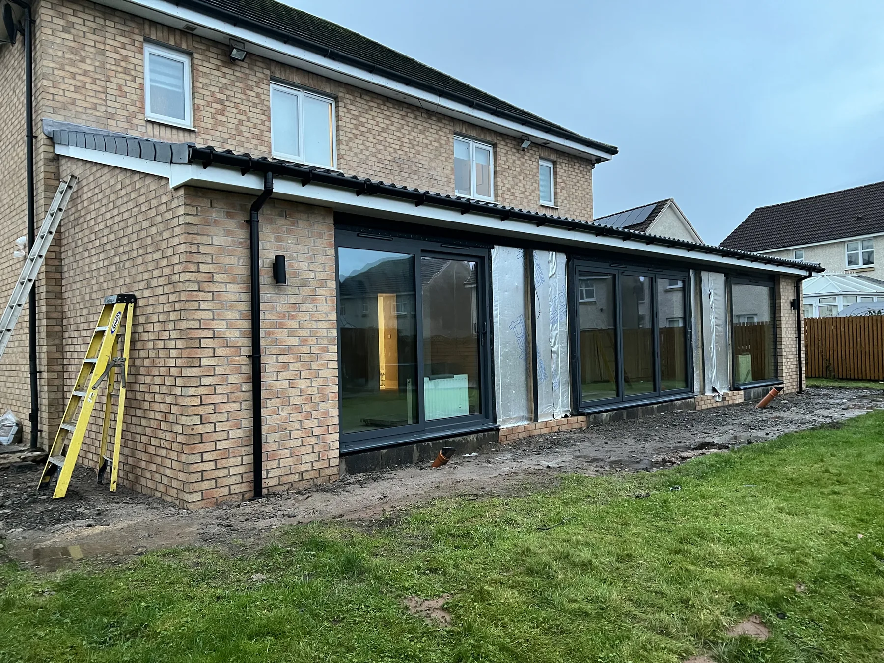 Long rear extension with dark framed glazing and unfinished ground outside